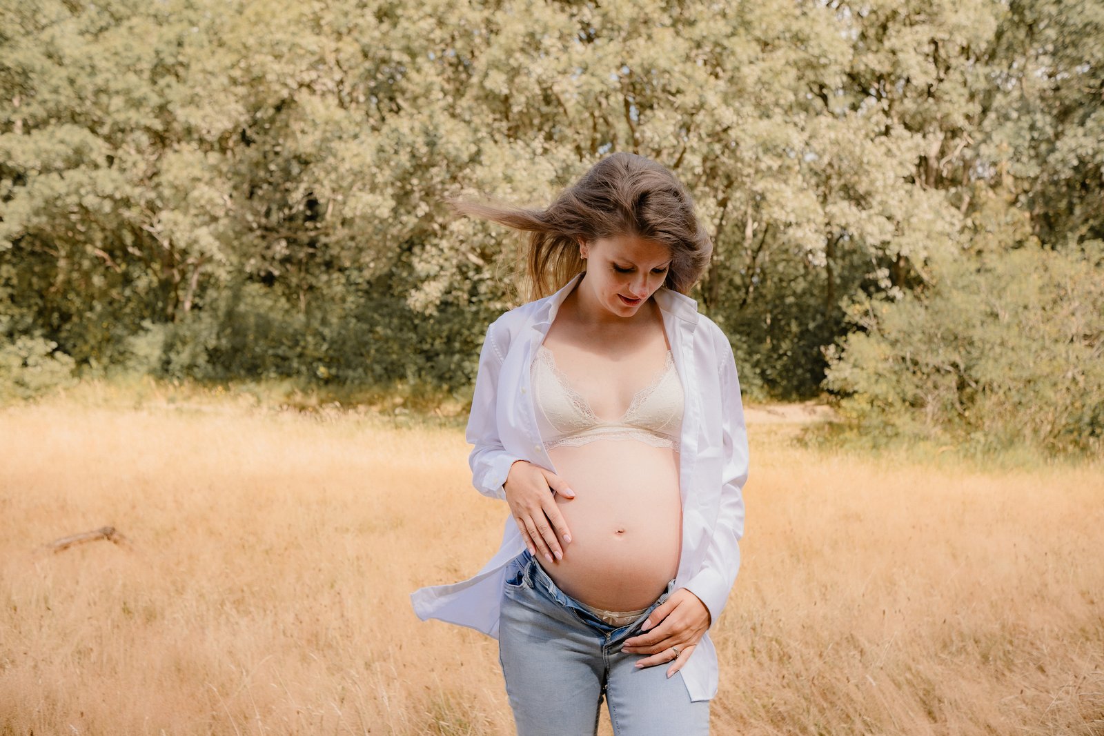 Zwangere vrouw staand in het veld, handen op haar buik